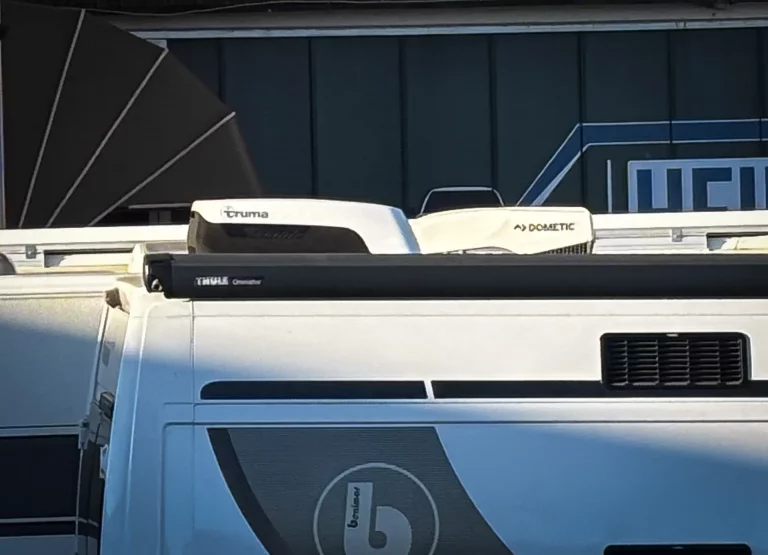 White van roof with two rooftop units (Truma on left, Dometic on right) mounted on a roof rack.